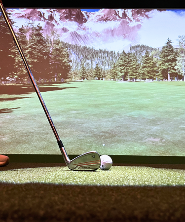 A modern golf simulator setup with a large screen, golf clubs, and a player swinging in a well-lit indoor space.
